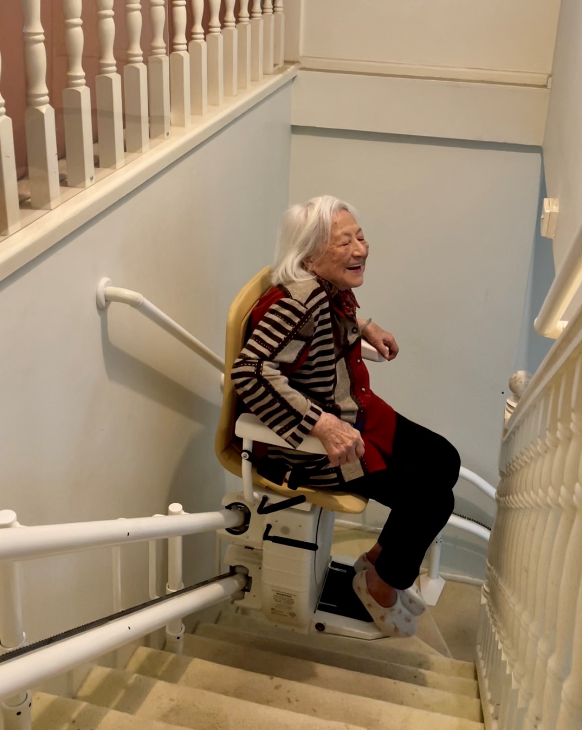 An elderly woman riding an indoor stair lift.